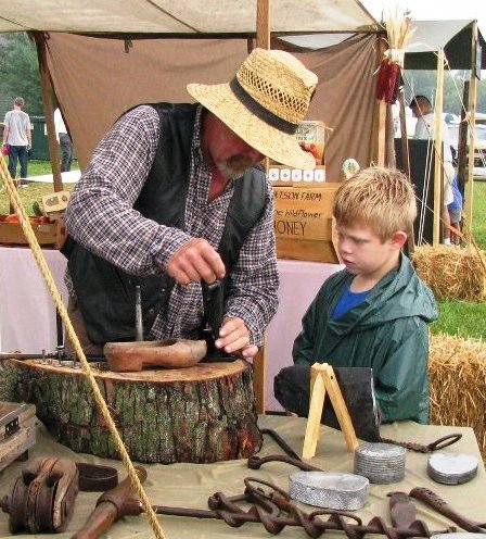 An elder showing a young boy a traditional craft at an outdoor fair