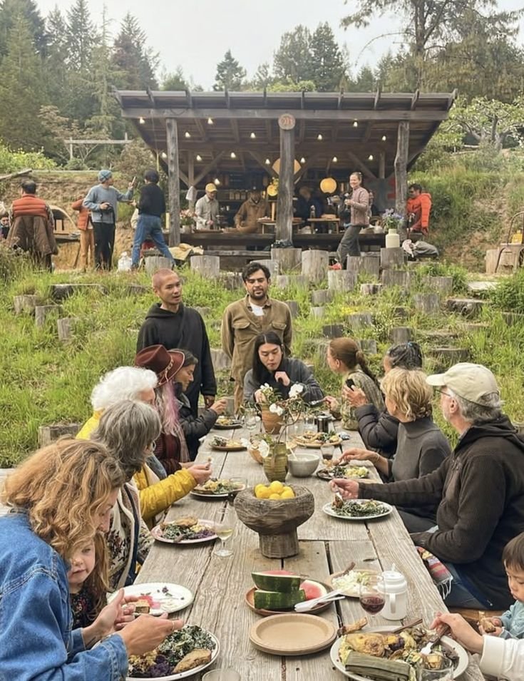 Neighbors of all ages sharing a long outdoor meal under the trees